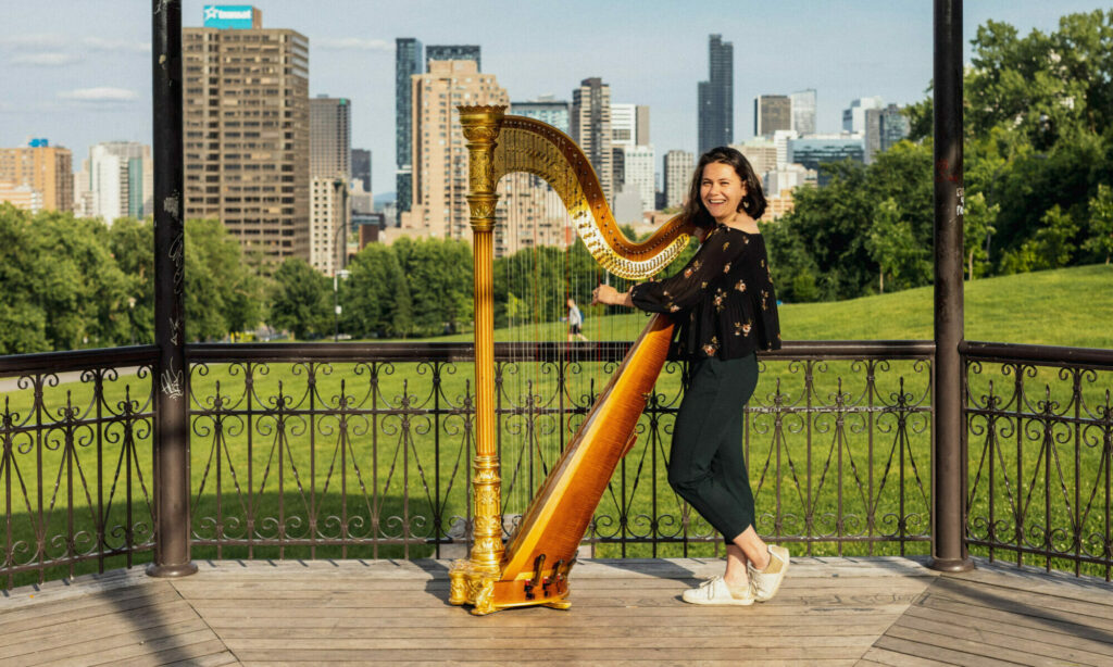 Femme posant derrière une harpe avec la ville de Montréal en fond.